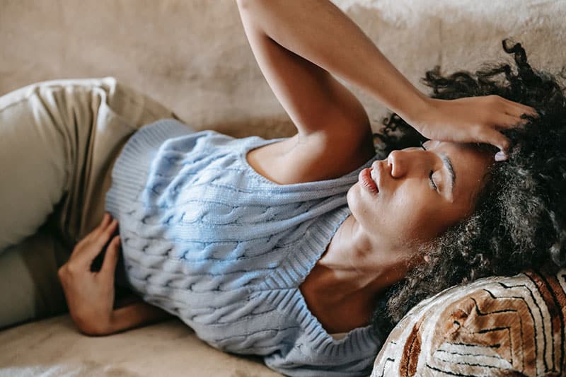 woman lying down on couch, appearing unwell