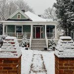 a pretty house covered in snow, as seen from a high angle above brick gate entryway