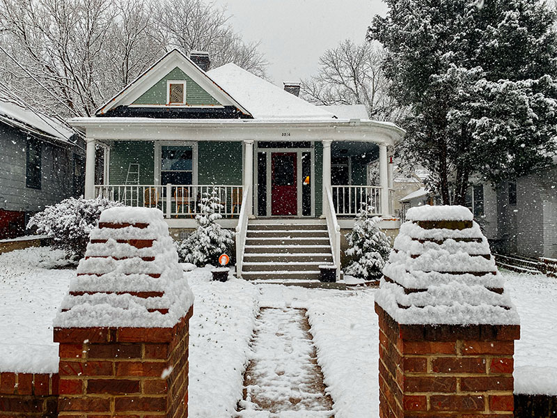 a pretty house covered in snow, as seen from a high angle above brick gate entryway