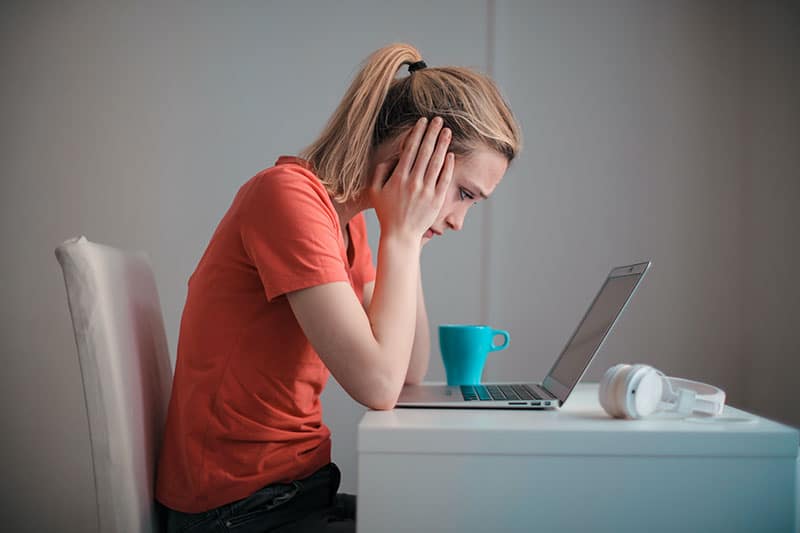 young woman looking at laptop on a desk, frustrated, seen from the side